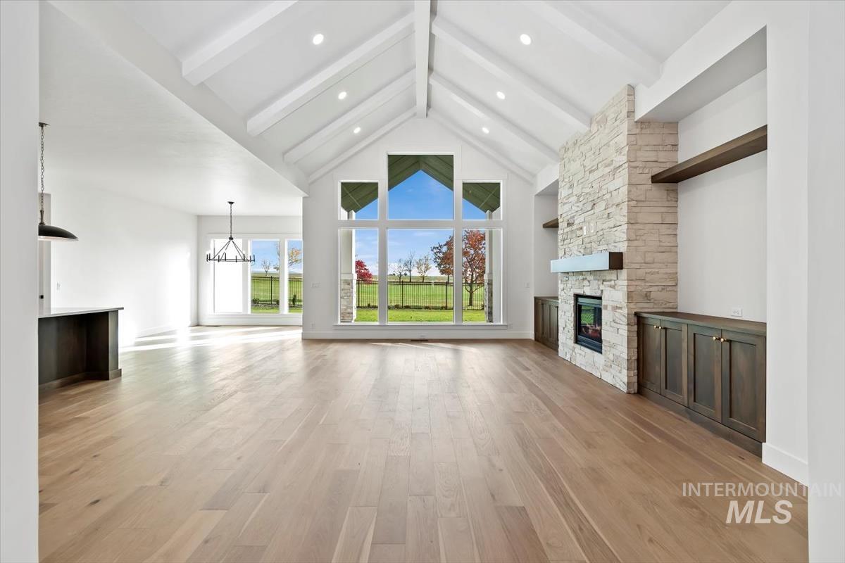 Unfurnished living room with light wood finished floors, beam ceiling, a stone fireplace, plenty of natural light, and high vaulted ceiling