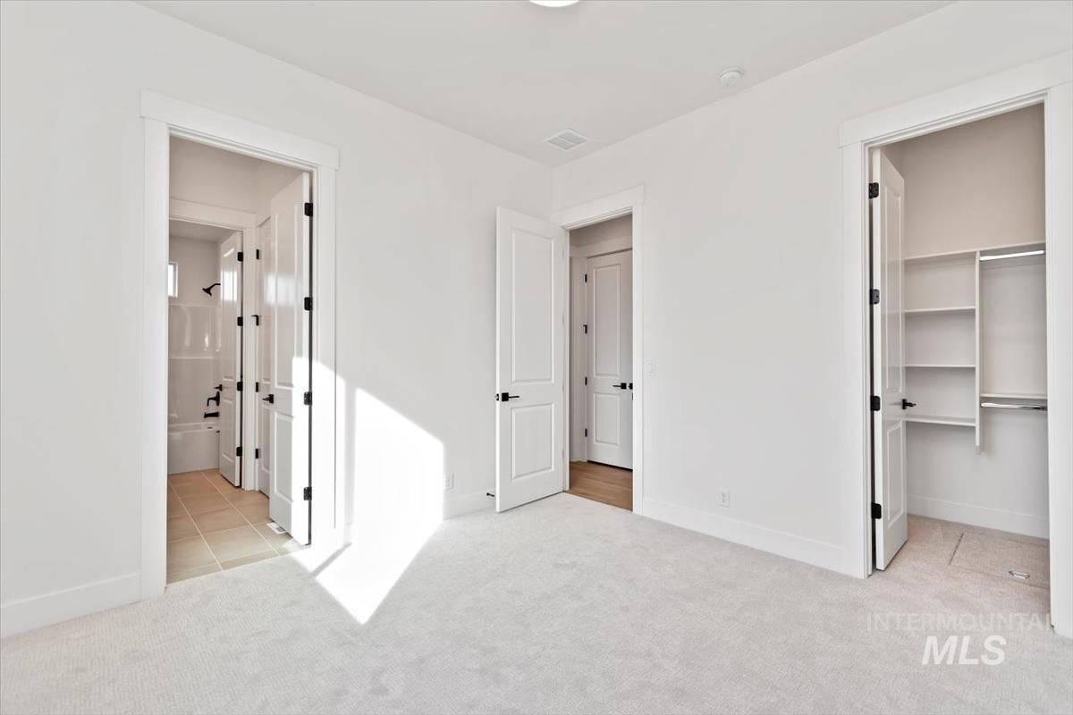 Unfurnished bedroom with a walk in closet, light carpet, ensuite bath, and light tile patterned floors