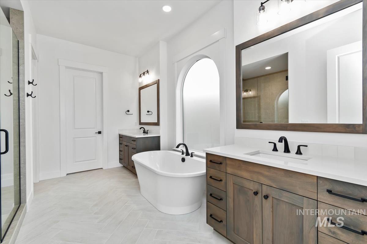 Bathroom featuring a freestanding bath, two vanities, a stall shower, and recessed lighting