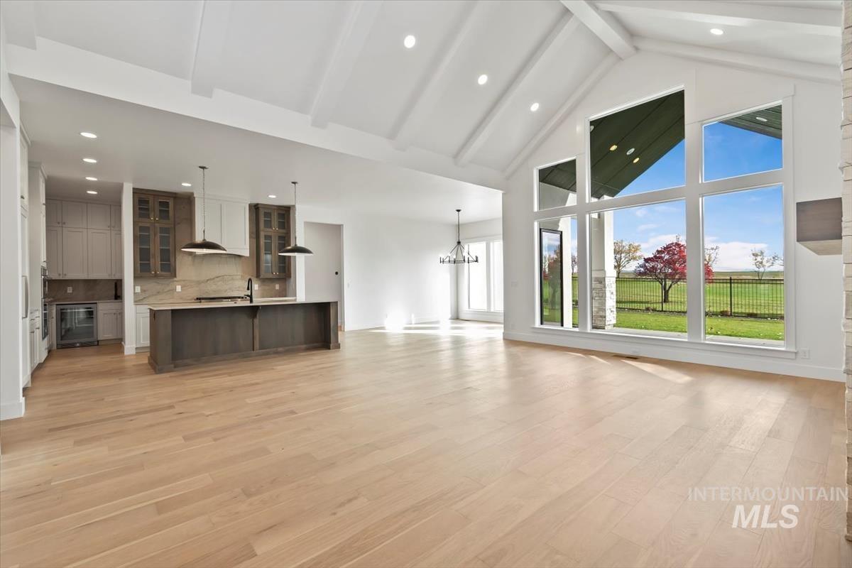 Unfurnished living room with high vaulted ceiling, beamed ceiling, light wood-style floors, recessed lighting, and a chandelier