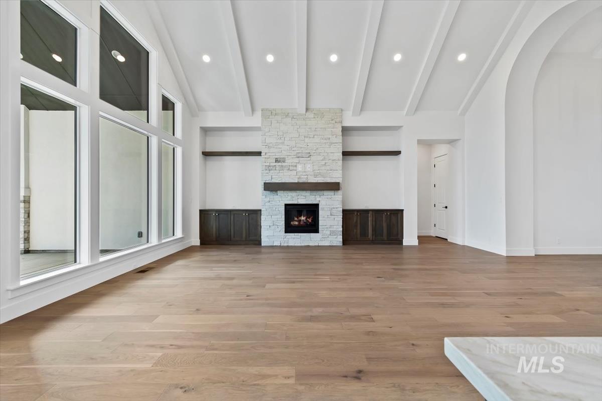 Unfurnished living room featuring light wood-style floors, a fireplace, recessed lighting, arched walkways, and beam ceiling