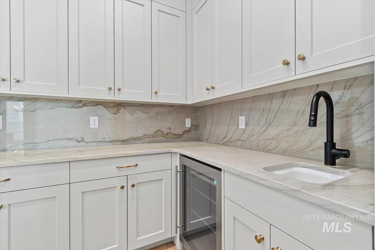 Kitchen with beverage cooler, white cabinets, light stone countertops, and backsplash