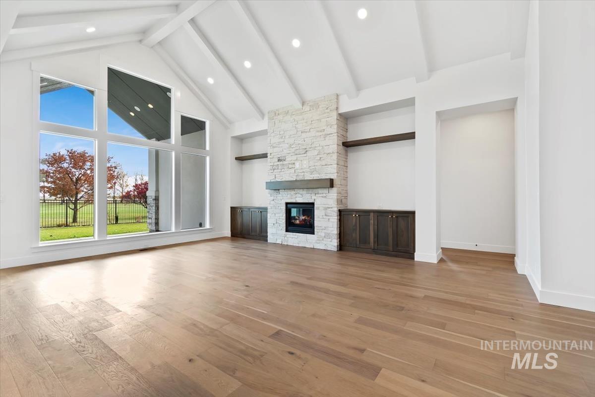Unfurnished living room featuring beam ceiling, light wood-style flooring, a stone fireplace, high vaulted ceiling, and recessed lighting