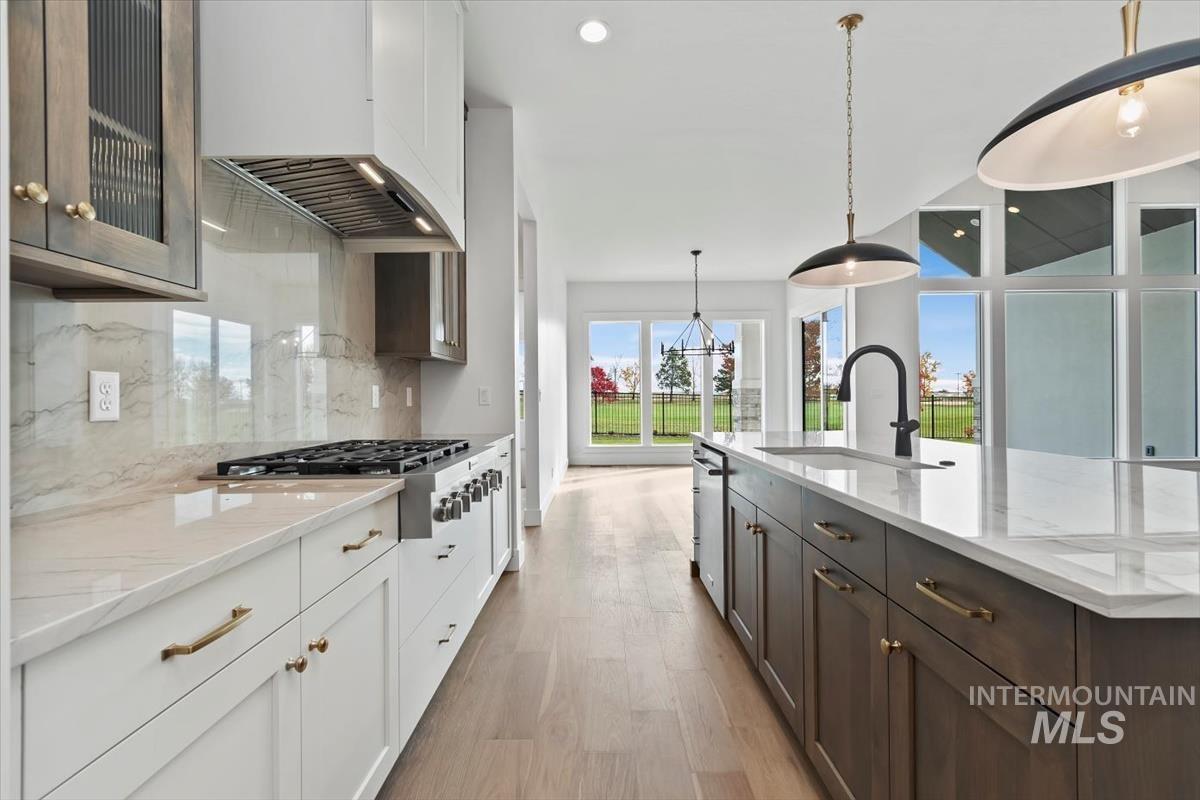 Kitchen featuring dark brown cabinetry, white cabinetry, light stone countertops, pendant lighting, and light wood-style floors