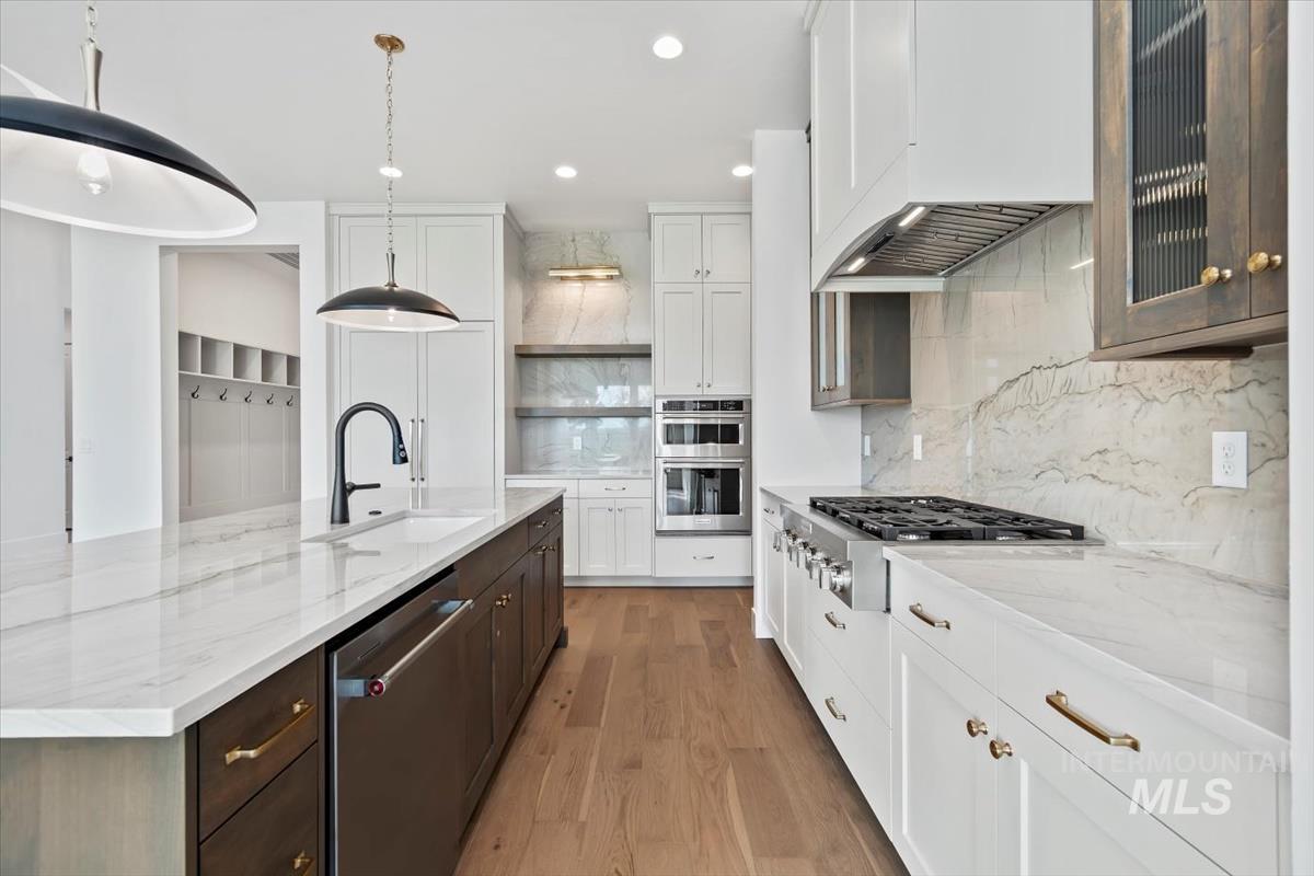 Kitchen with light stone counters, light wood-type flooring, stainless steel appliances, a center island with sink, and recessed lighting