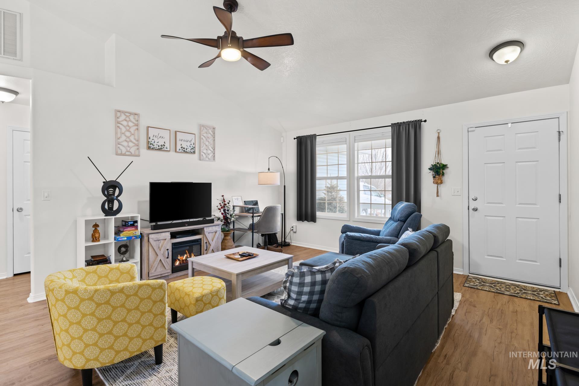 Living area with wood finished floors, ceiling fan, high vaulted ceiling, and a glass covered fireplace