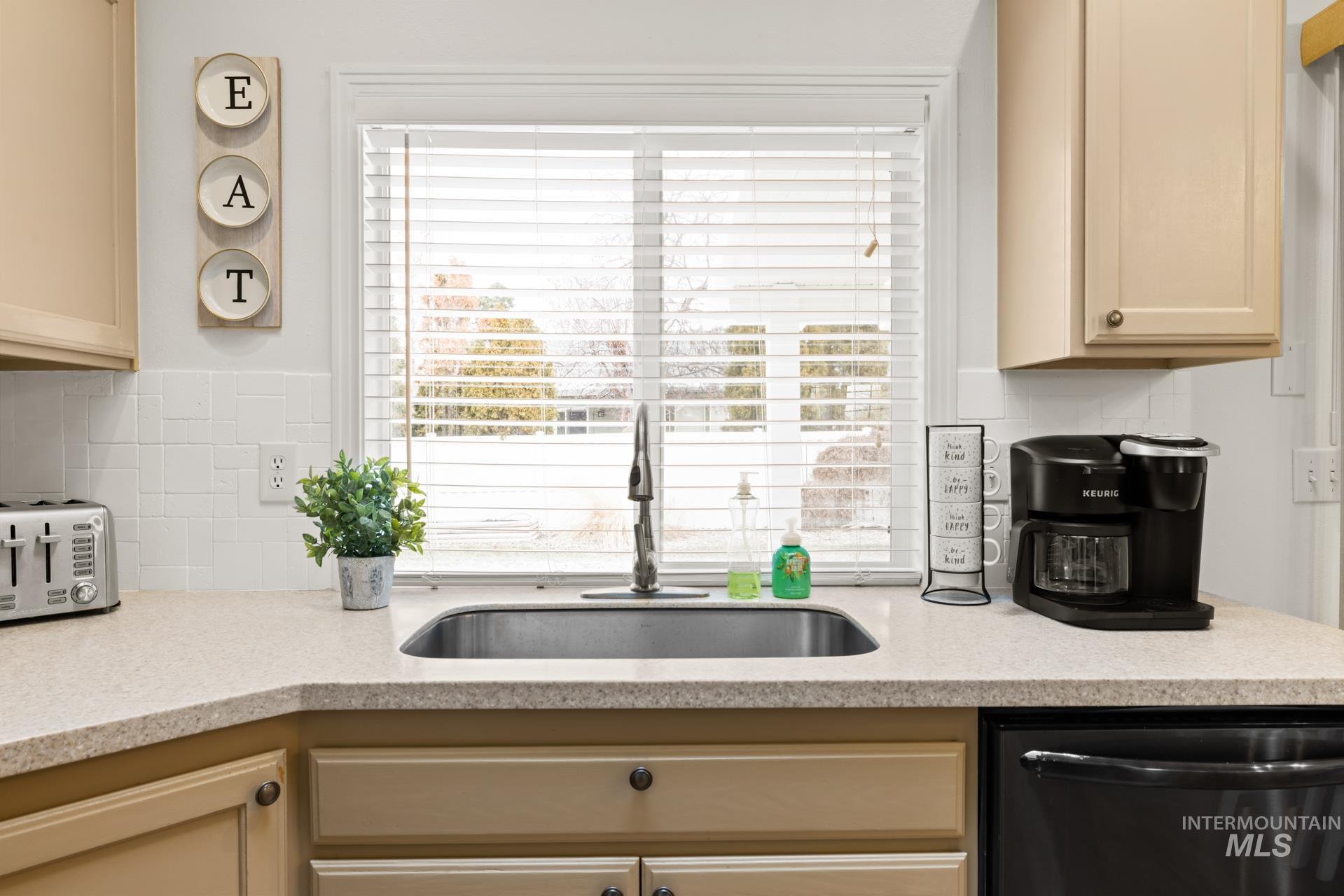 Kitchen with stainless steel dishwasher, tasteful backsplash, light stone counters, and cream cabinets