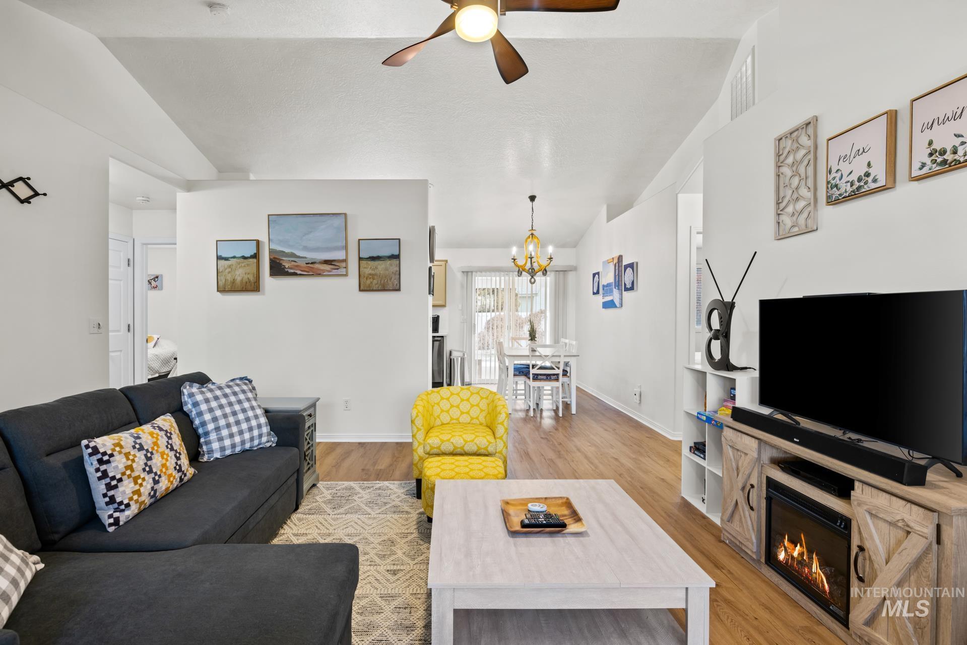 Living room featuring a glass covered fireplace, light wood-type flooring, lofted ceiling, ceiling fan, and a chandelier