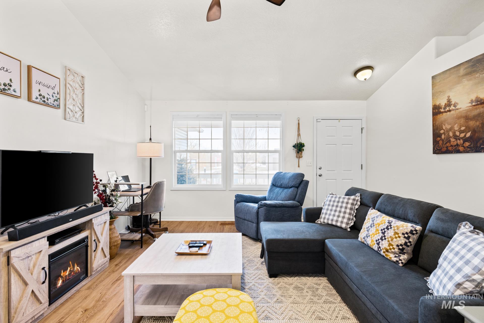 Living room featuring light wood-style floors, a glass covered fireplace, ceiling fan, and vaulted ceiling