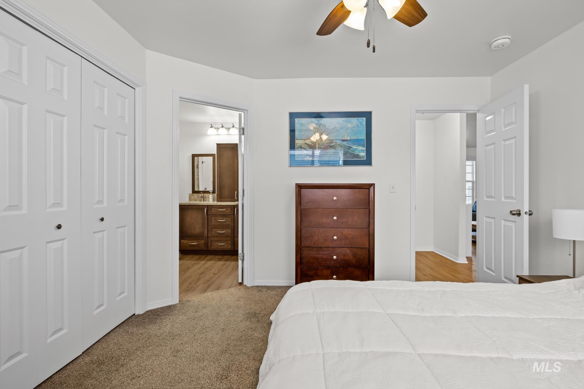 Carpeted bedroom featuring a closet, ensuite bathroom, and a ceiling fan