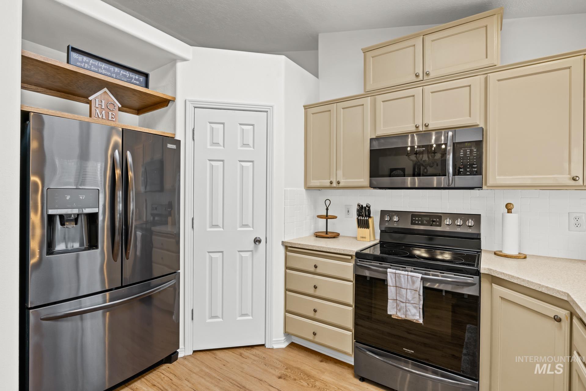 Kitchen with cream cabinets, appliances with stainless steel finishes, tasteful backsplash, light wood-style floors, and open shelves