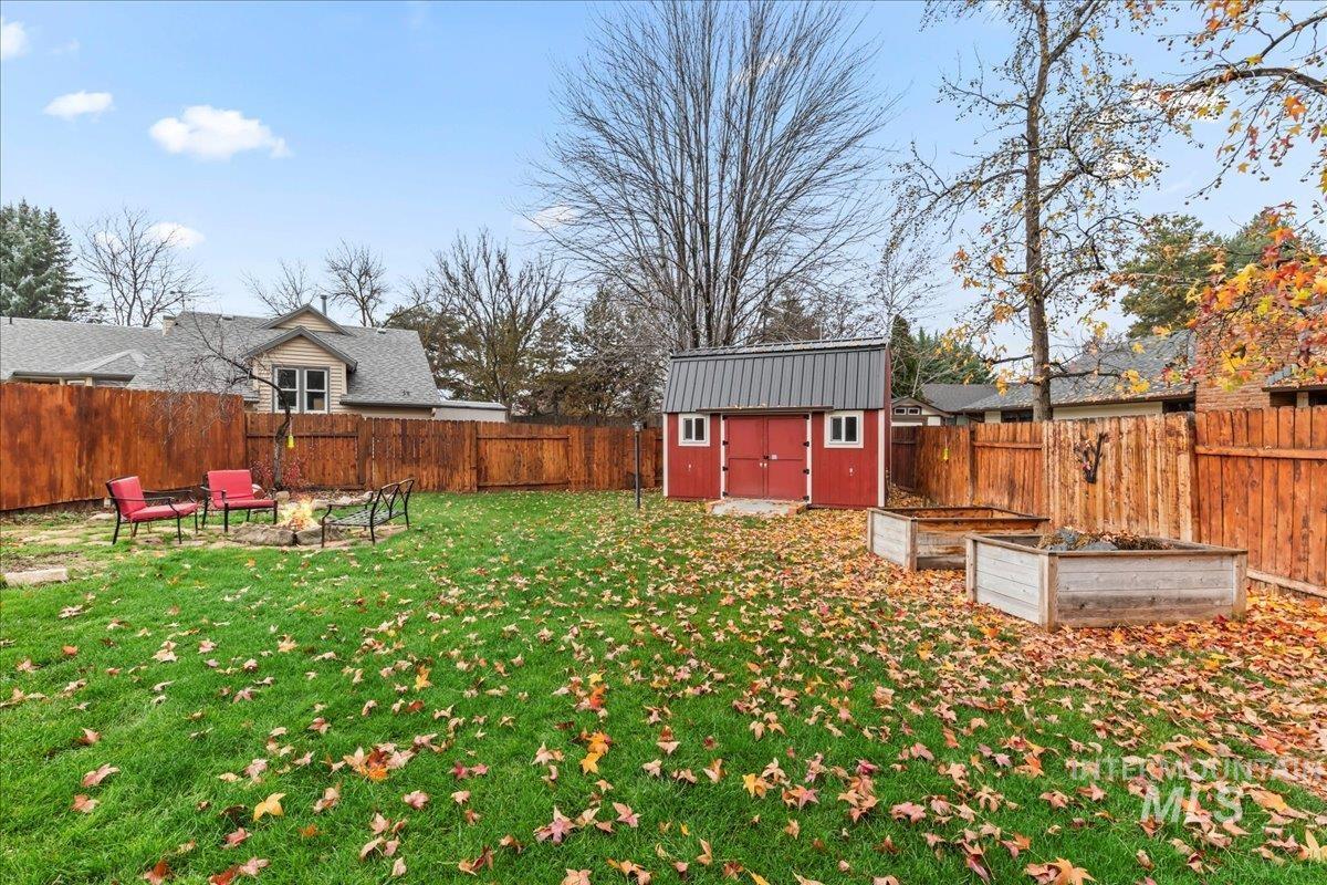 Fenced backyard with a garden, a storage shed, and an outdoor fire pit