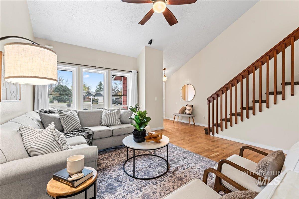 Living area with wood finished floors, a ceiling fan, and stairs
