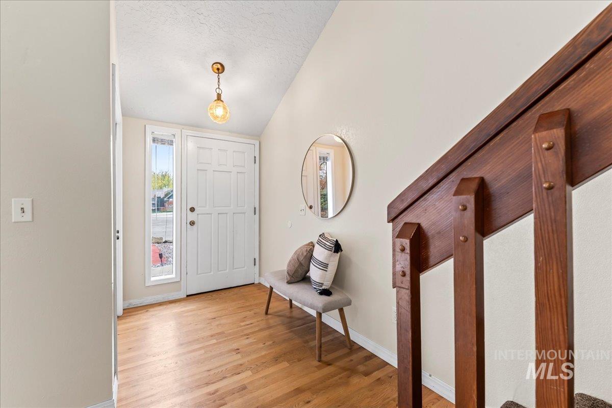 Entryway with a textured ceiling, light wood-style flooring, and lofted ceiling