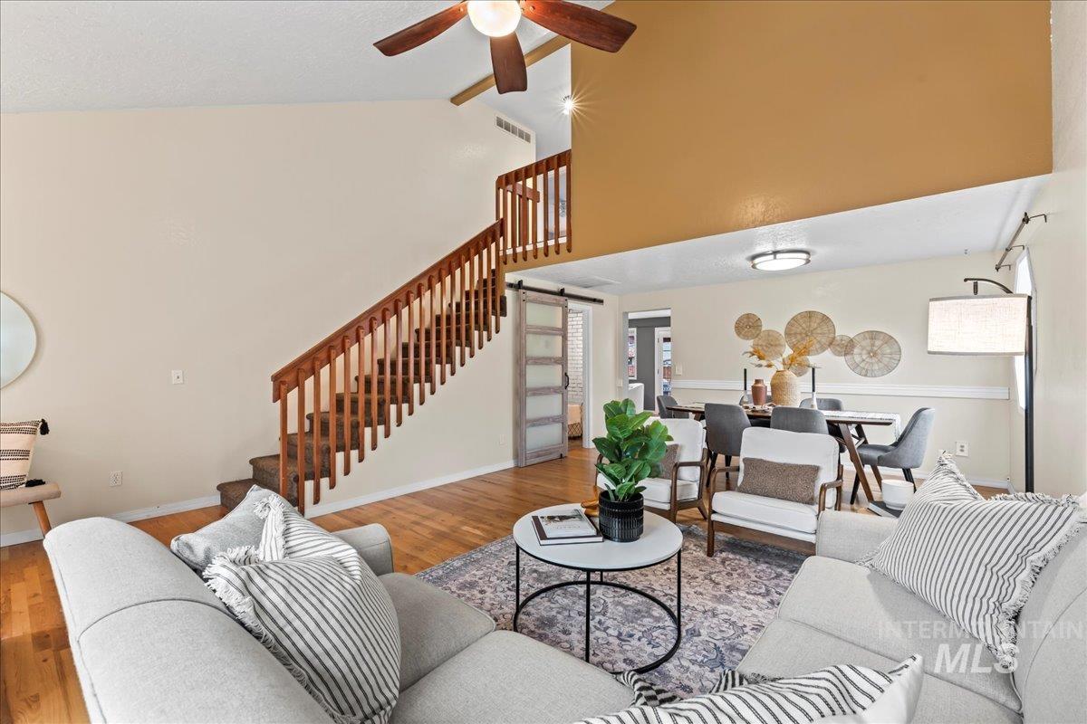 Living room featuring a barn door, stairway, wood finished floors, high vaulted ceiling, and beamed ceiling
