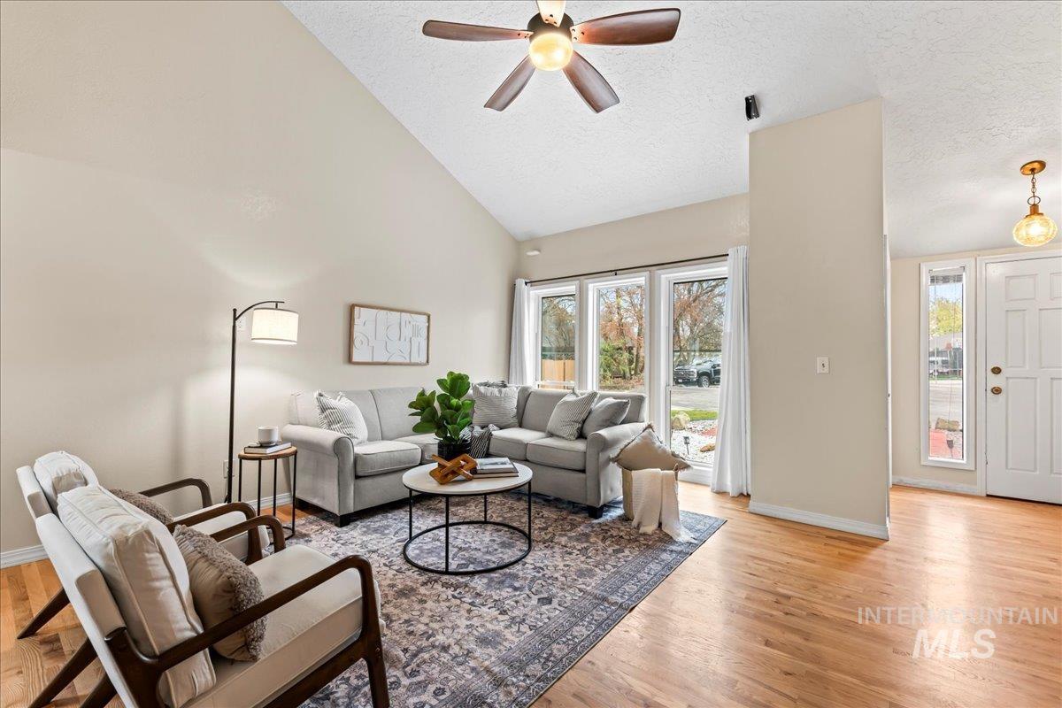 Living room with a textured ceiling, light wood-type flooring, high vaulted ceiling, and ceiling fan