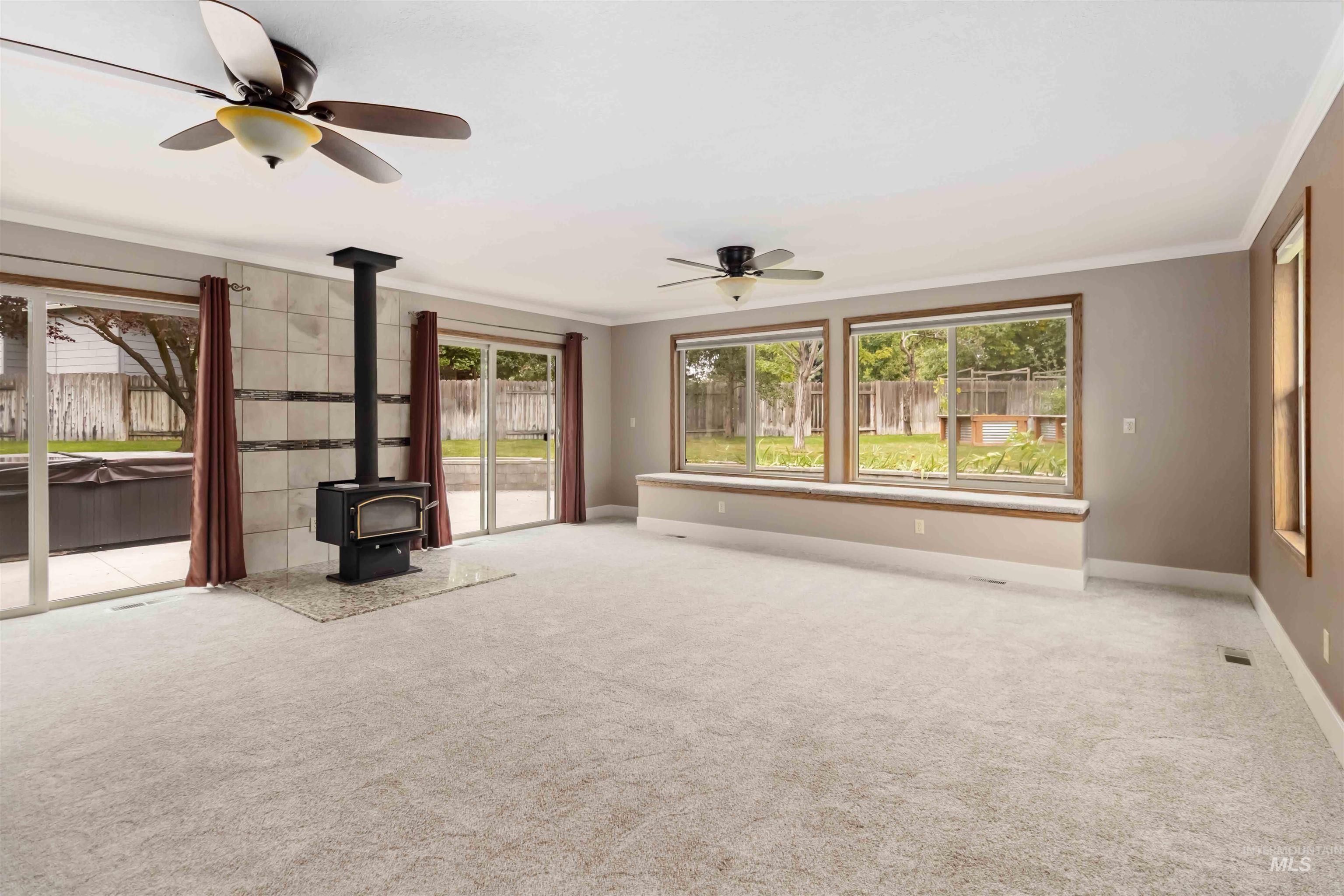 Unfurnished living room with a wood stove, light colored carpet, crown molding, and a ceiling fan
