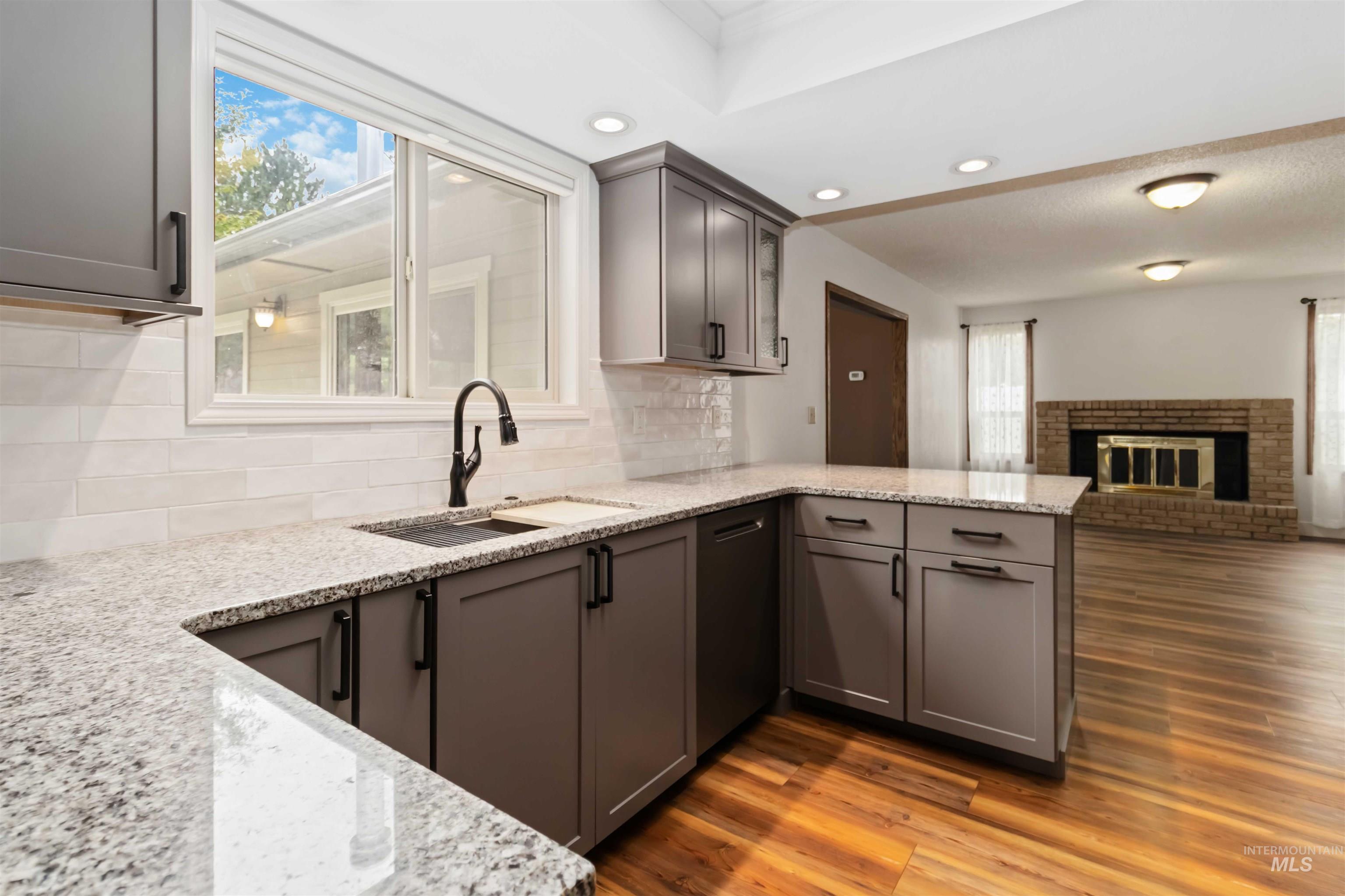 Kitchen with gray cabinetry, light stone counters, dark wood-style flooring, decorative backsplash, and a brick fireplace