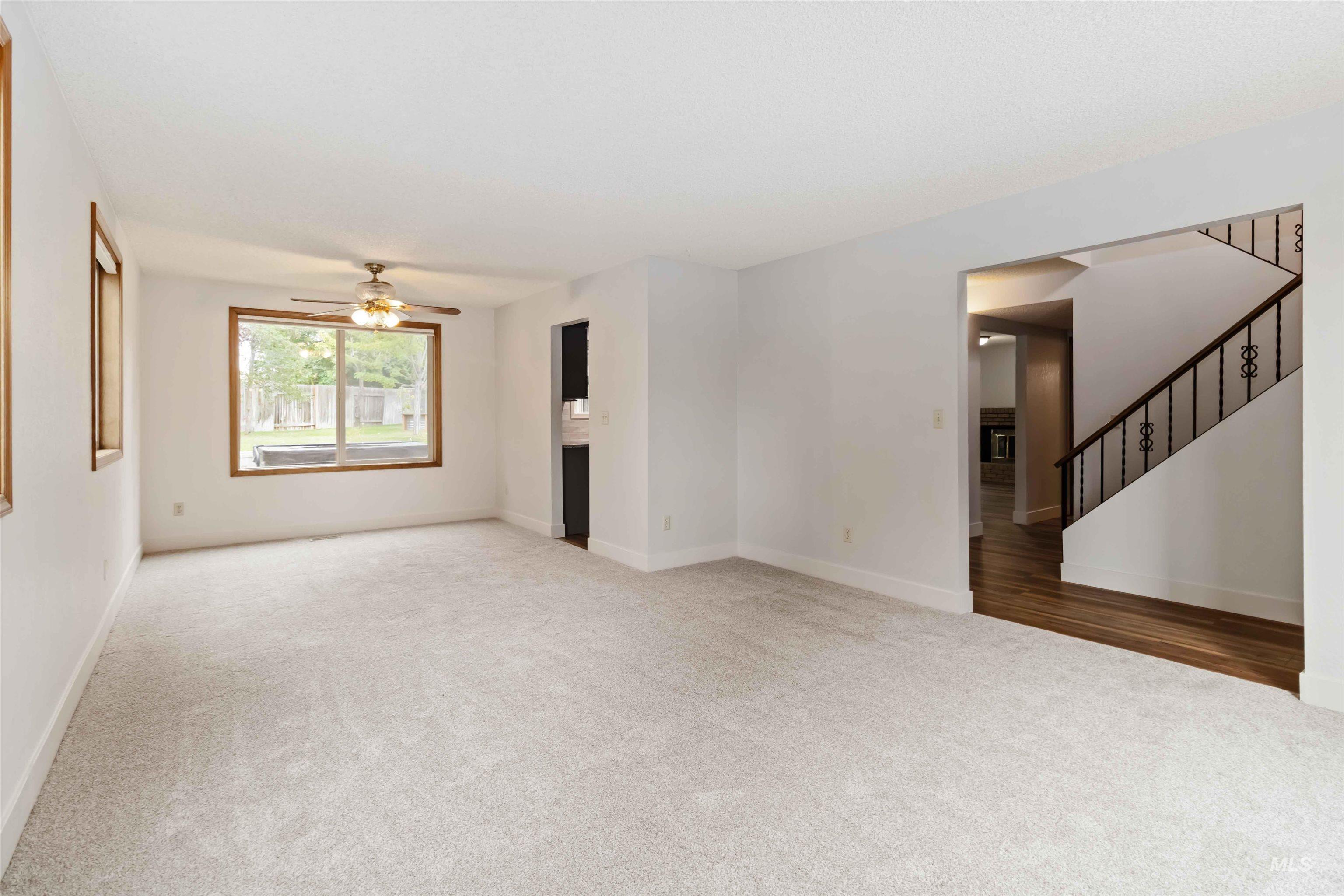 Unfurnished living room with light carpet, stairway, and a ceiling fan
