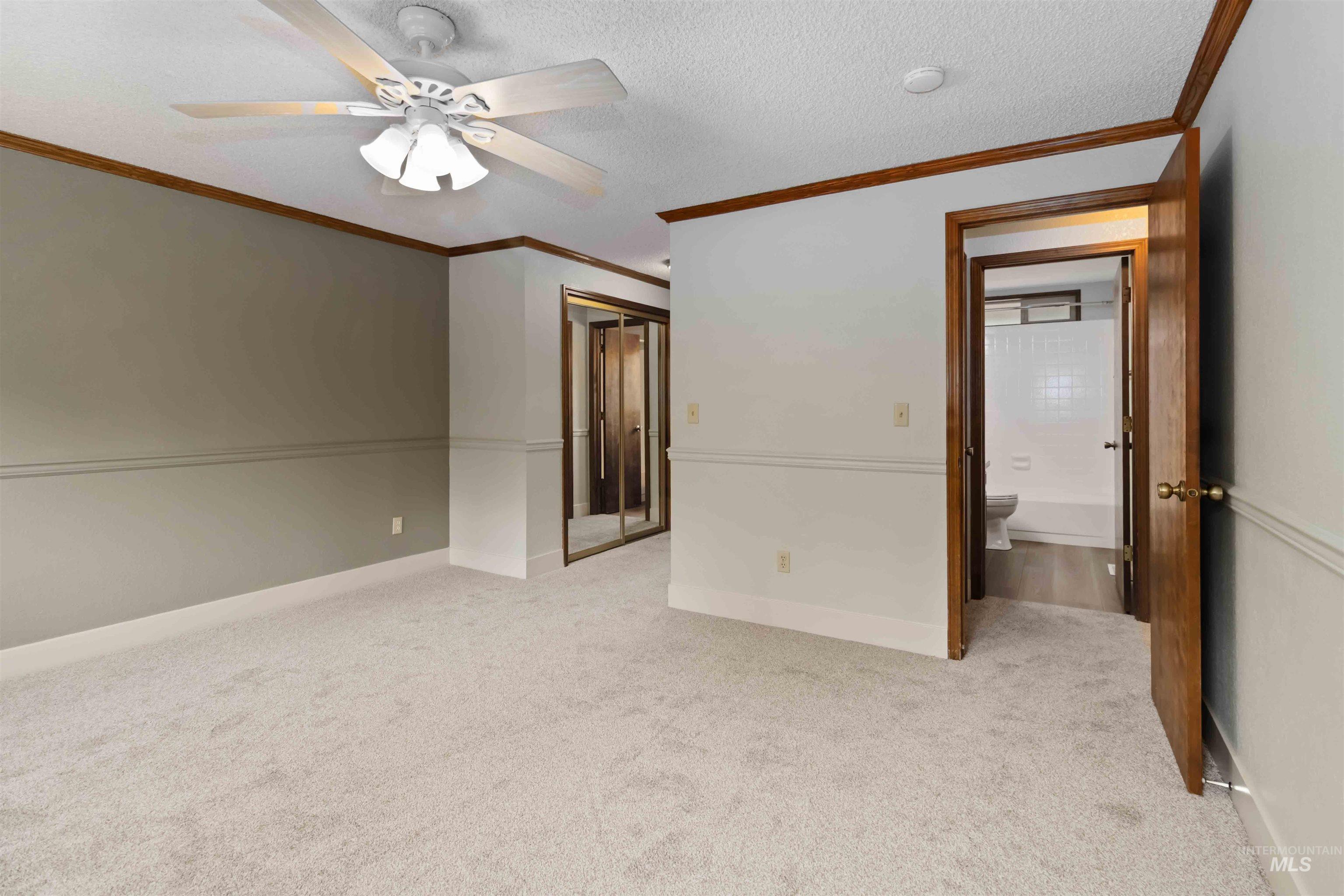 Unfurnished bedroom with a textured ceiling, ornamental molding, a closet, light colored carpet, and ceiling fan