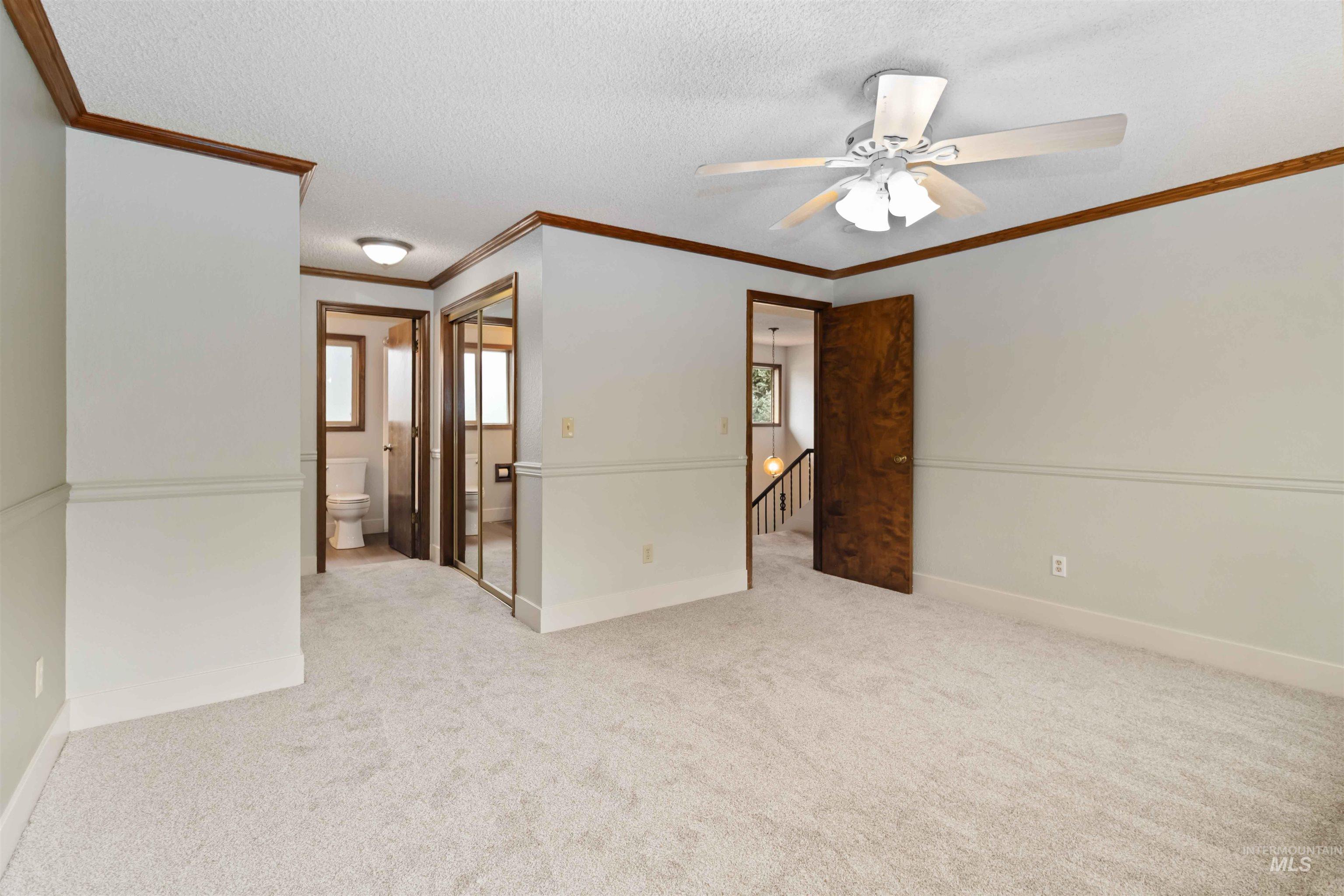 Spare room featuring a textured ceiling, light carpet, ornamental molding, and a ceiling fan
