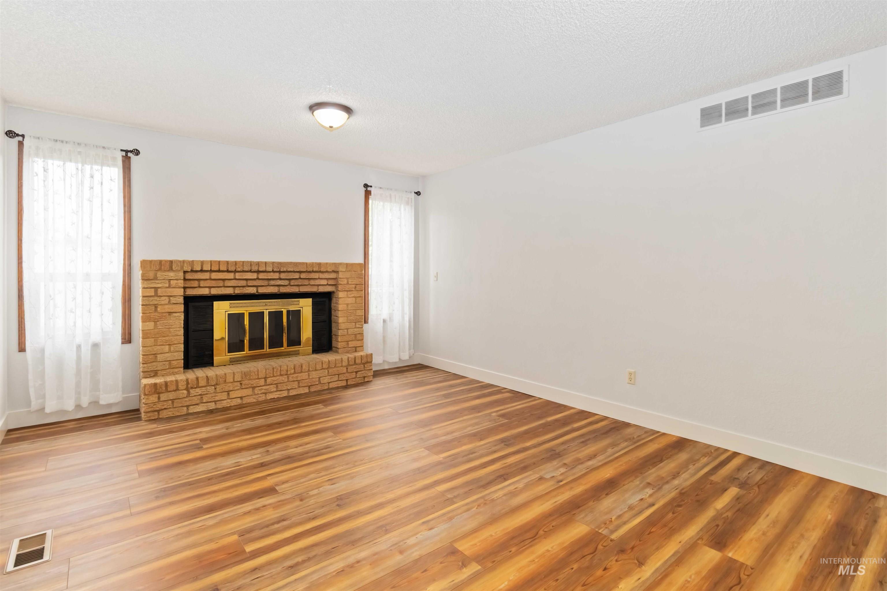 Unfurnished living room with a brick fireplace, wood finished floors, plenty of natural light, and a textured ceiling