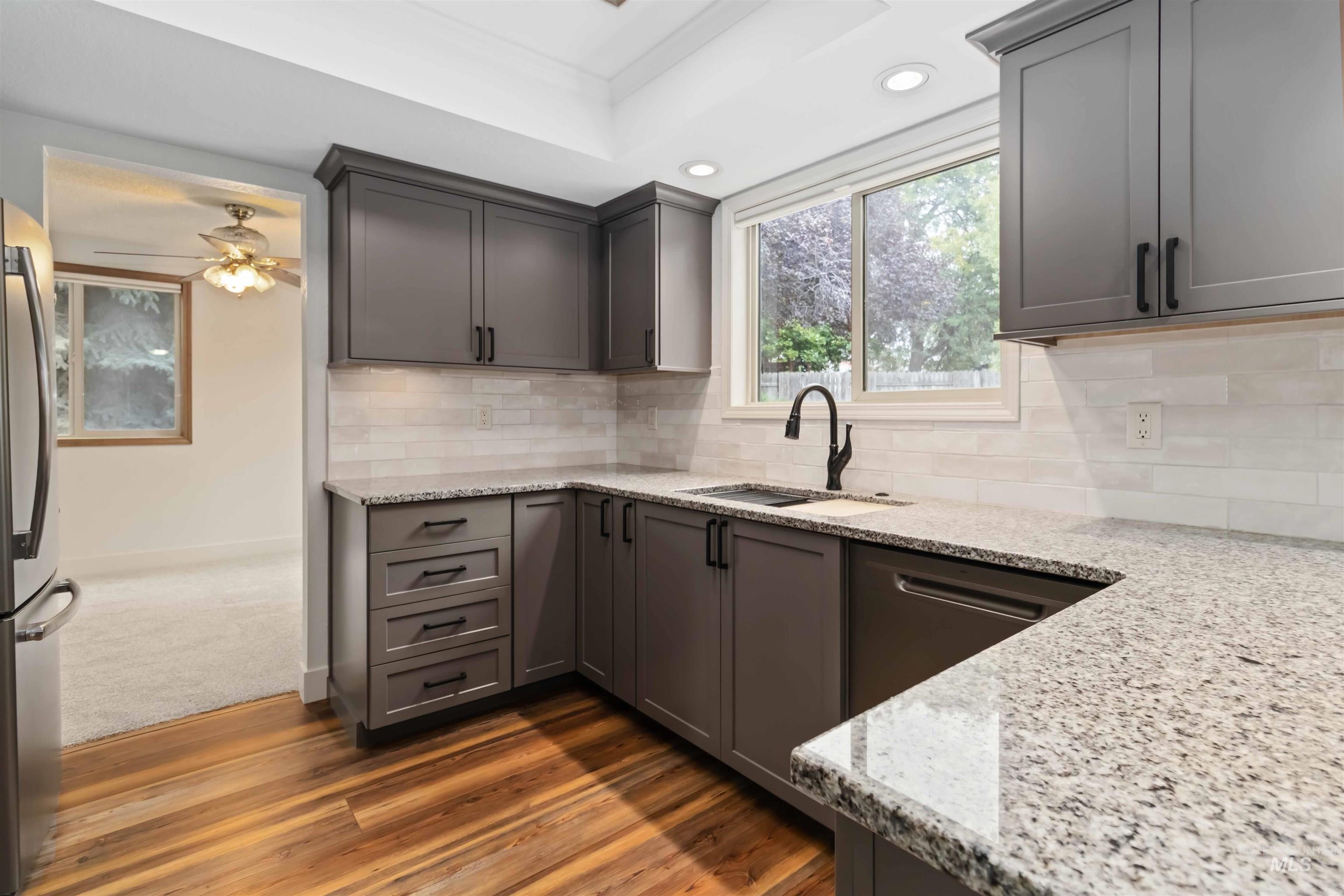 Kitchen featuring gray cabinetry, light stone counters, dark wood-style flooring, freestanding refrigerator, and tasteful backsplash
