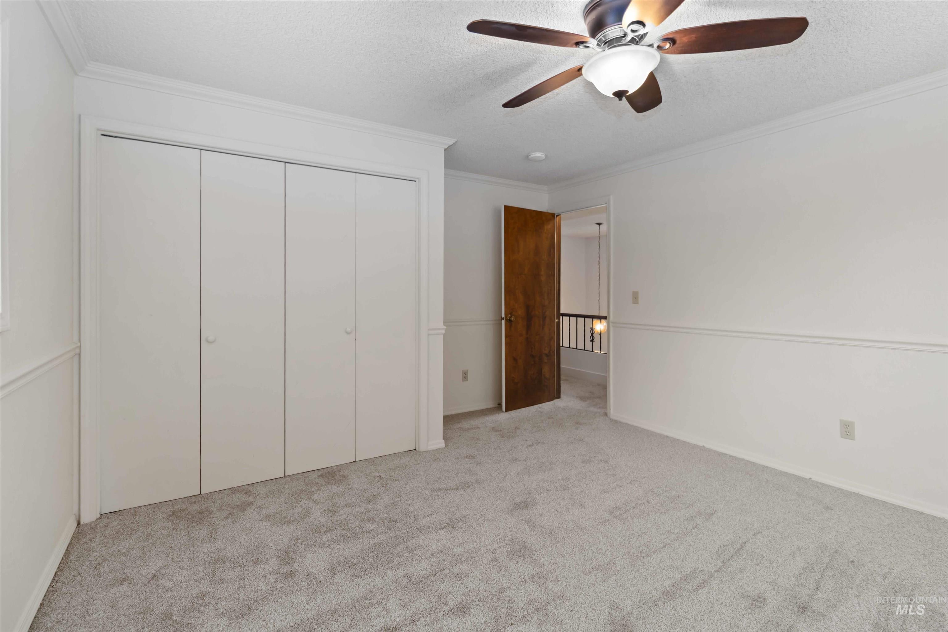 Unfurnished bedroom with ornamental molding, light carpet, a textured ceiling, ceiling fan, and a closet