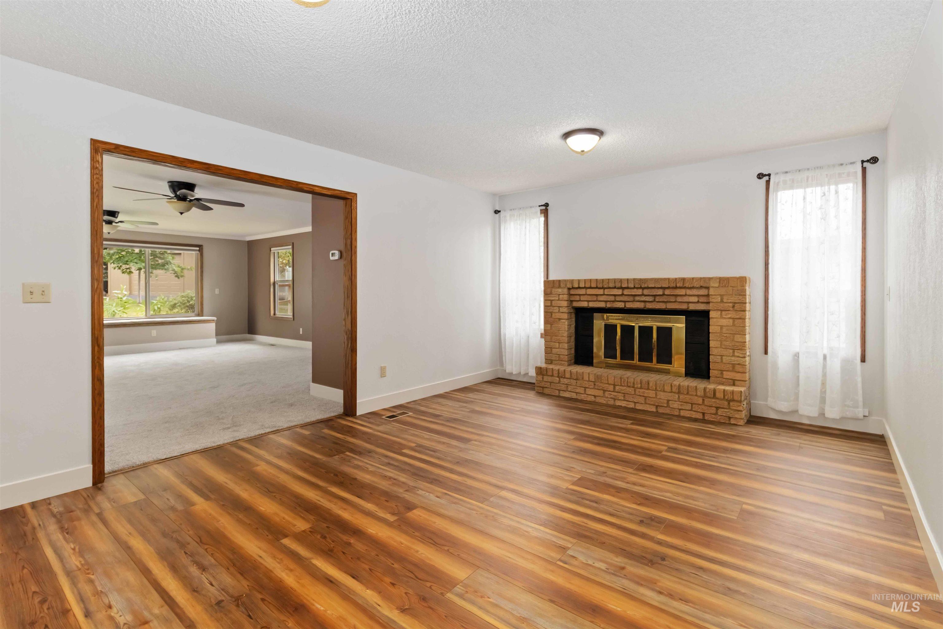 Unfurnished living room featuring a brick fireplace, light wood-style flooring, a textured ceiling, and a ceiling fan