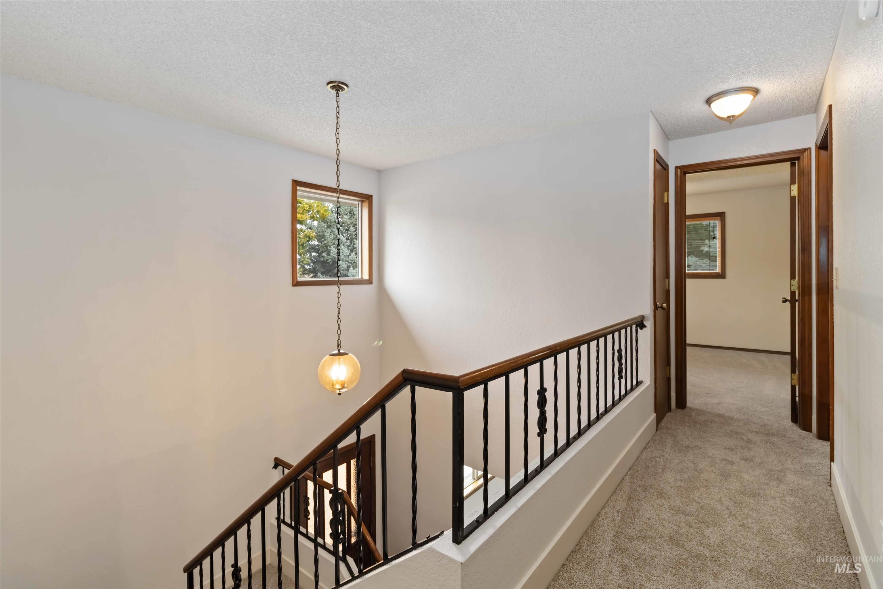 Corridor featuring light colored carpet, a textured ceiling, and an upstairs landing