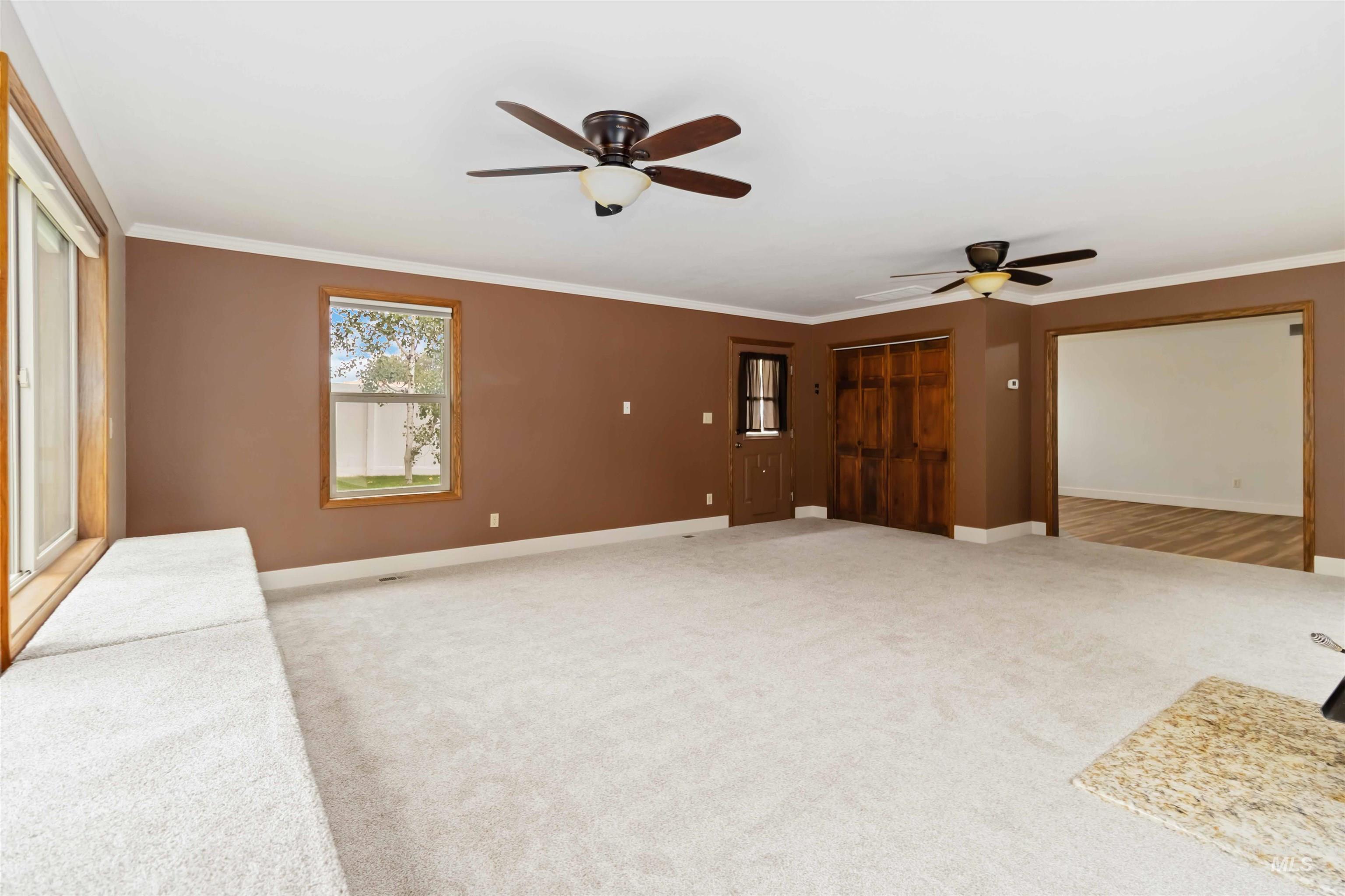 Unfurnished living room with ornamental molding, light colored carpet, and a ceiling fan