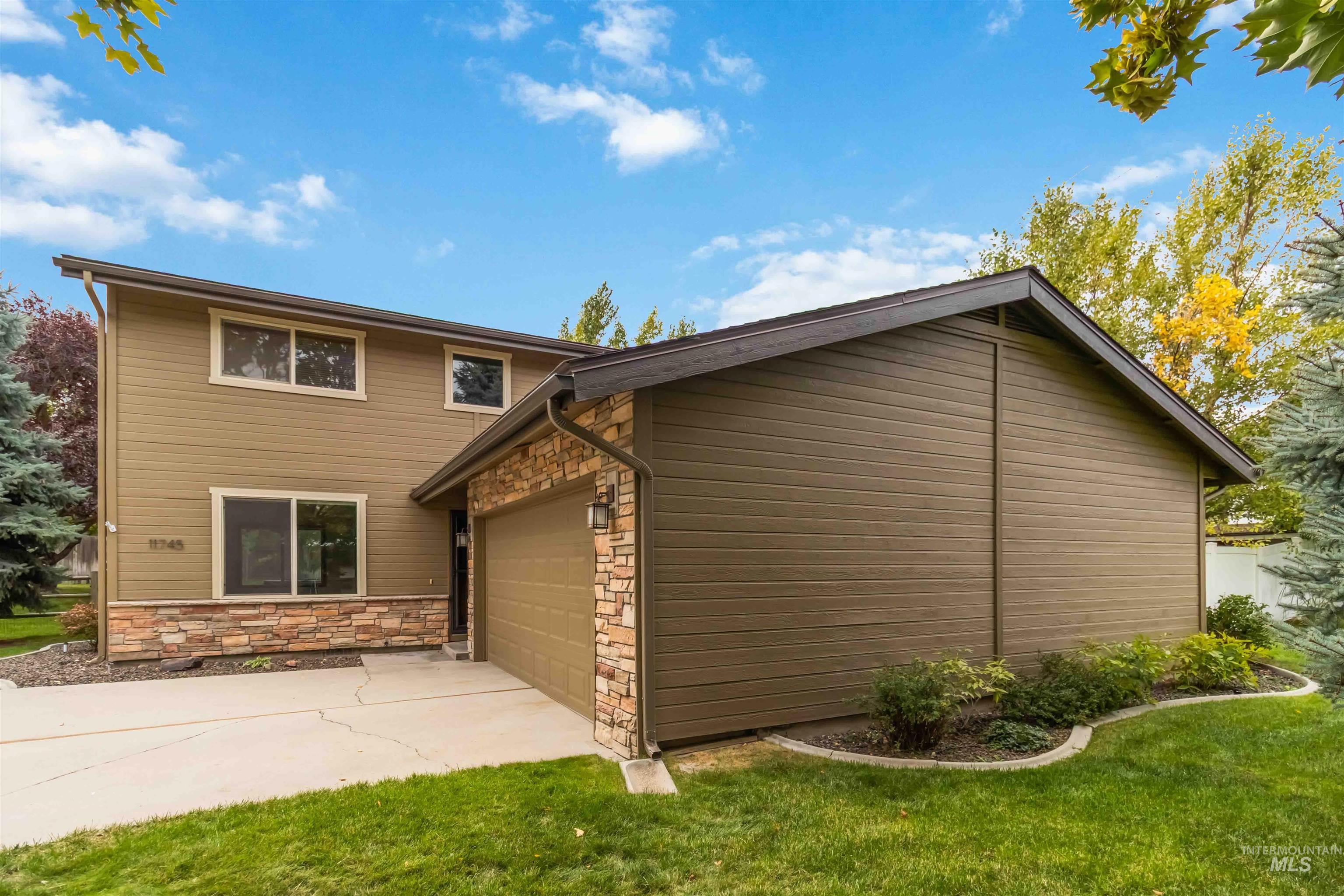 View of side of home with stone siding, a garage, concrete driveway, and a lawn