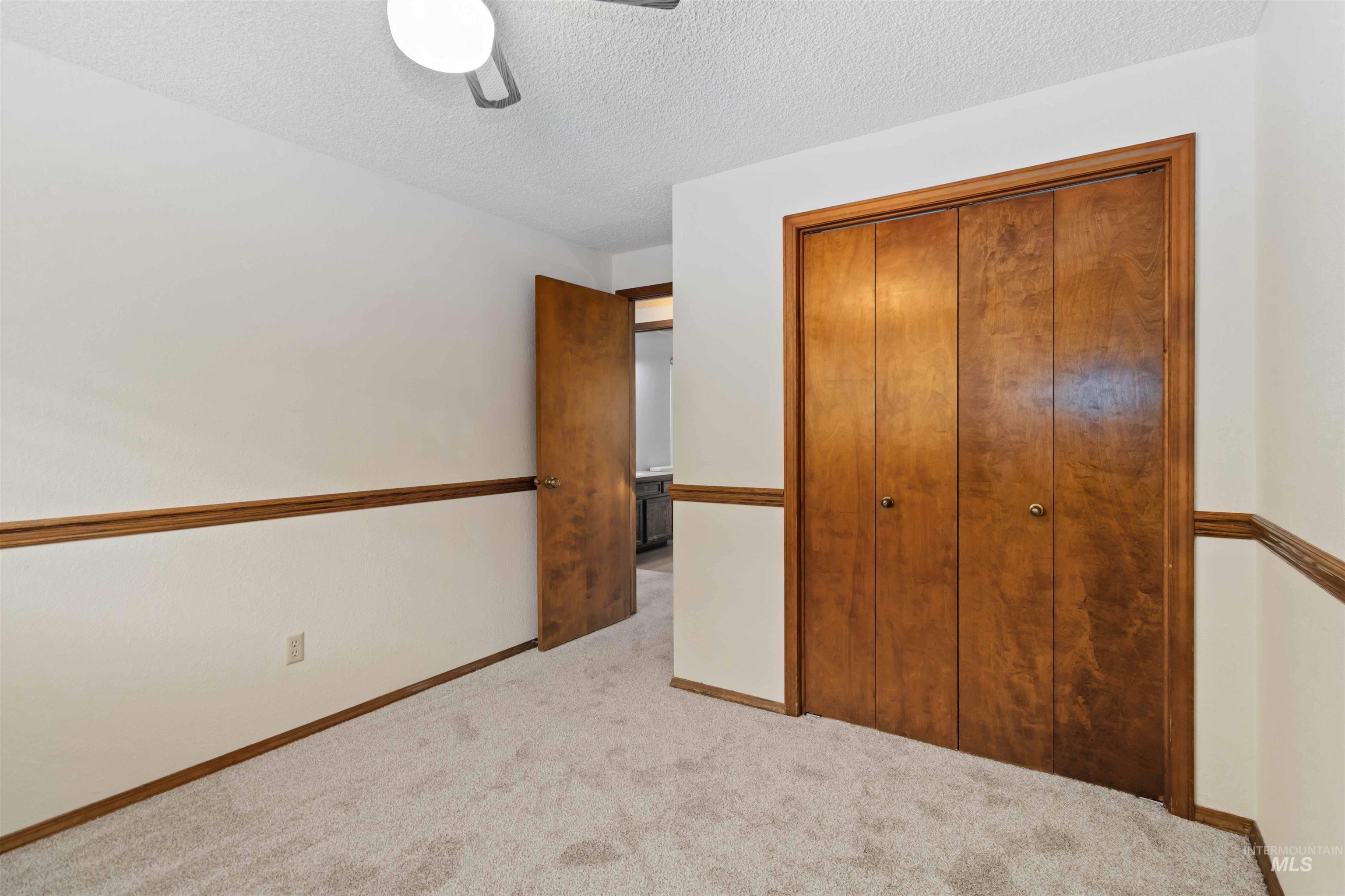 Unfurnished bedroom with a textured ceiling, light carpet, a closet, and a ceiling fan