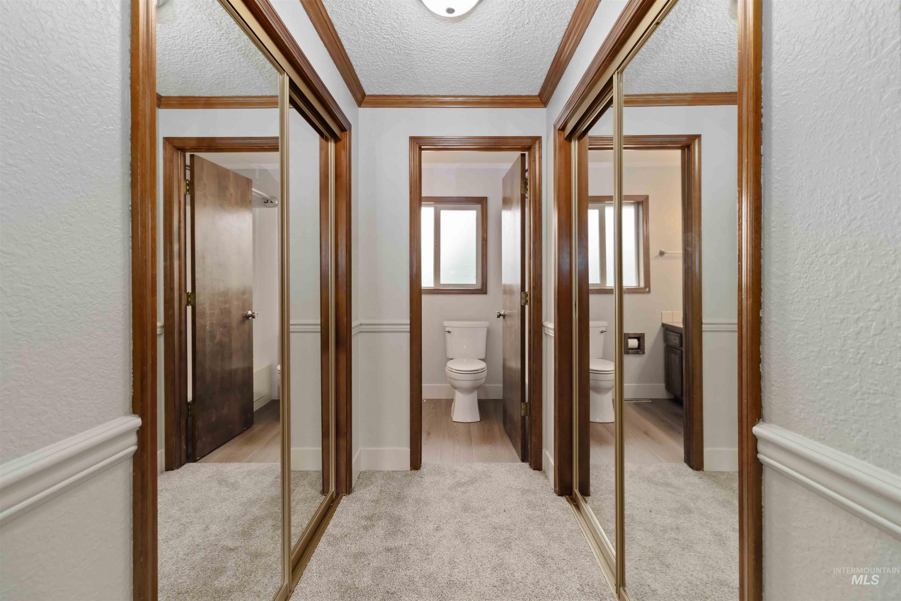 Corridor featuring a textured wall, a textured ceiling, ornamental molding, and light carpet