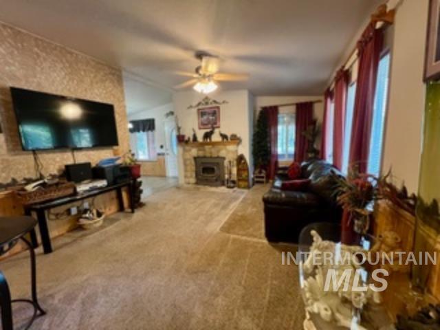 Carpeted living room featuring a fireplace, a ceiling fan, and vaulted ceiling
