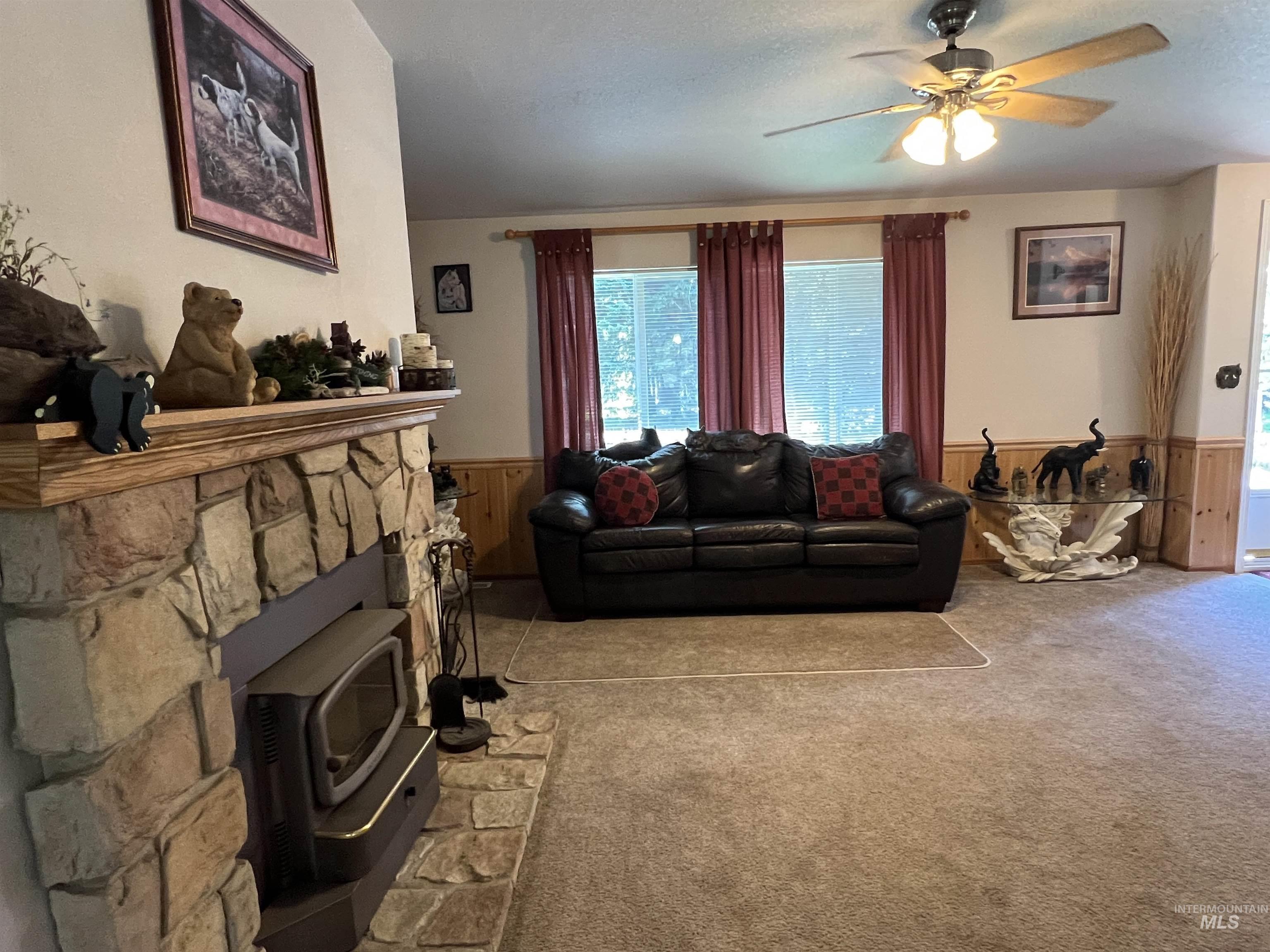 Living room featuring wainscoting, a ceiling fan, carpet flooring, wood walls, and a wood stove