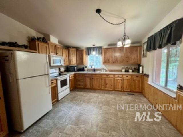 Kitchen featuring white appliances, a chandelier, light countertops, pendant lighting, and brown cabinetry