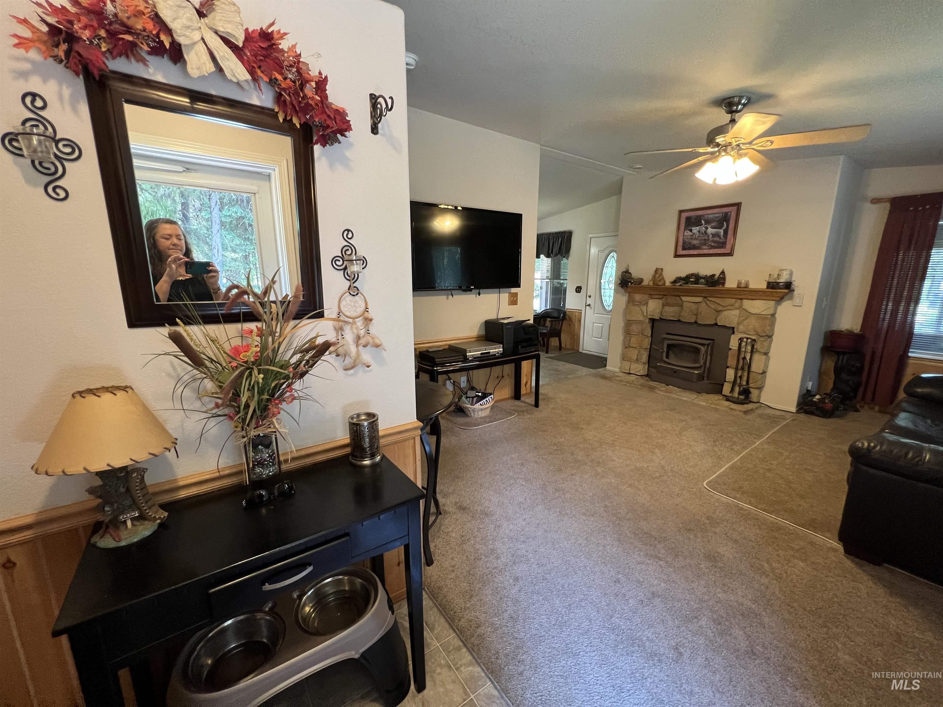 Living room with light carpet, healthy amount of natural light, a stone fireplace, and a ceiling fan