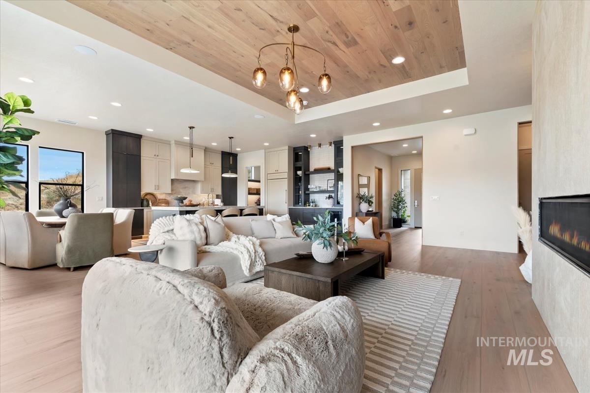 Living room with wooden ceiling, recessed lighting, a tray ceiling, light wood-style flooring, and a large fireplace