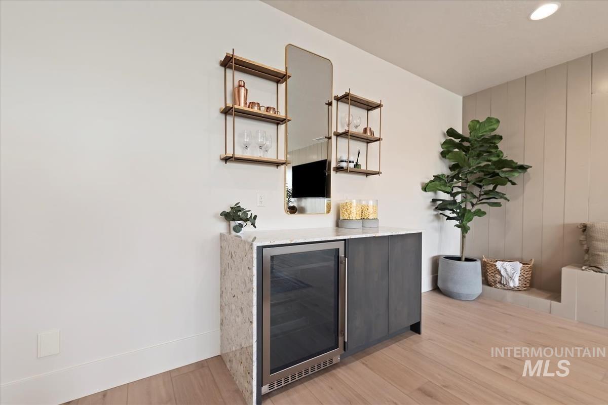 Bar area with wine cooler, light wood finished floors, light stone counters, open shelves, and modern cabinets