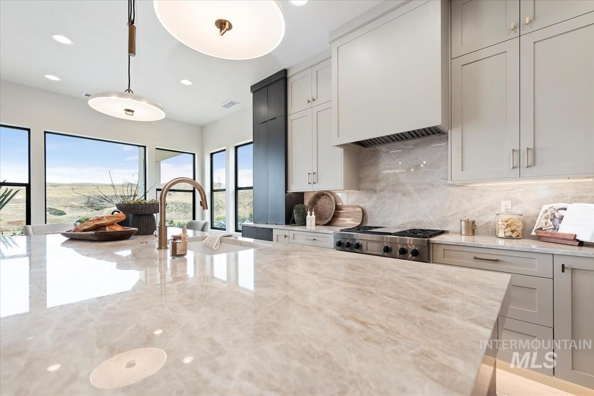 Kitchen featuring light stone counters, pendant lighting, decorative backsplash, custom range hood, and recessed lighting