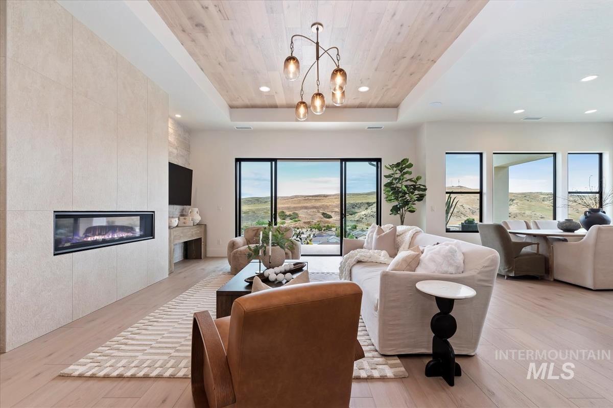 Living room with a raised ceiling, a tiled fireplace, light wood finished floors, wooden ceiling, and healthy amount of natural light