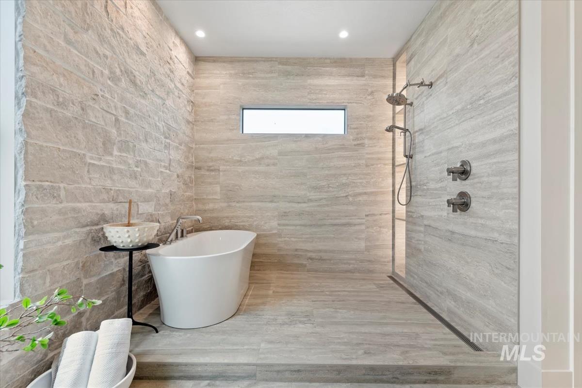Full bath featuring a freestanding bath, walk in shower, and tile walls