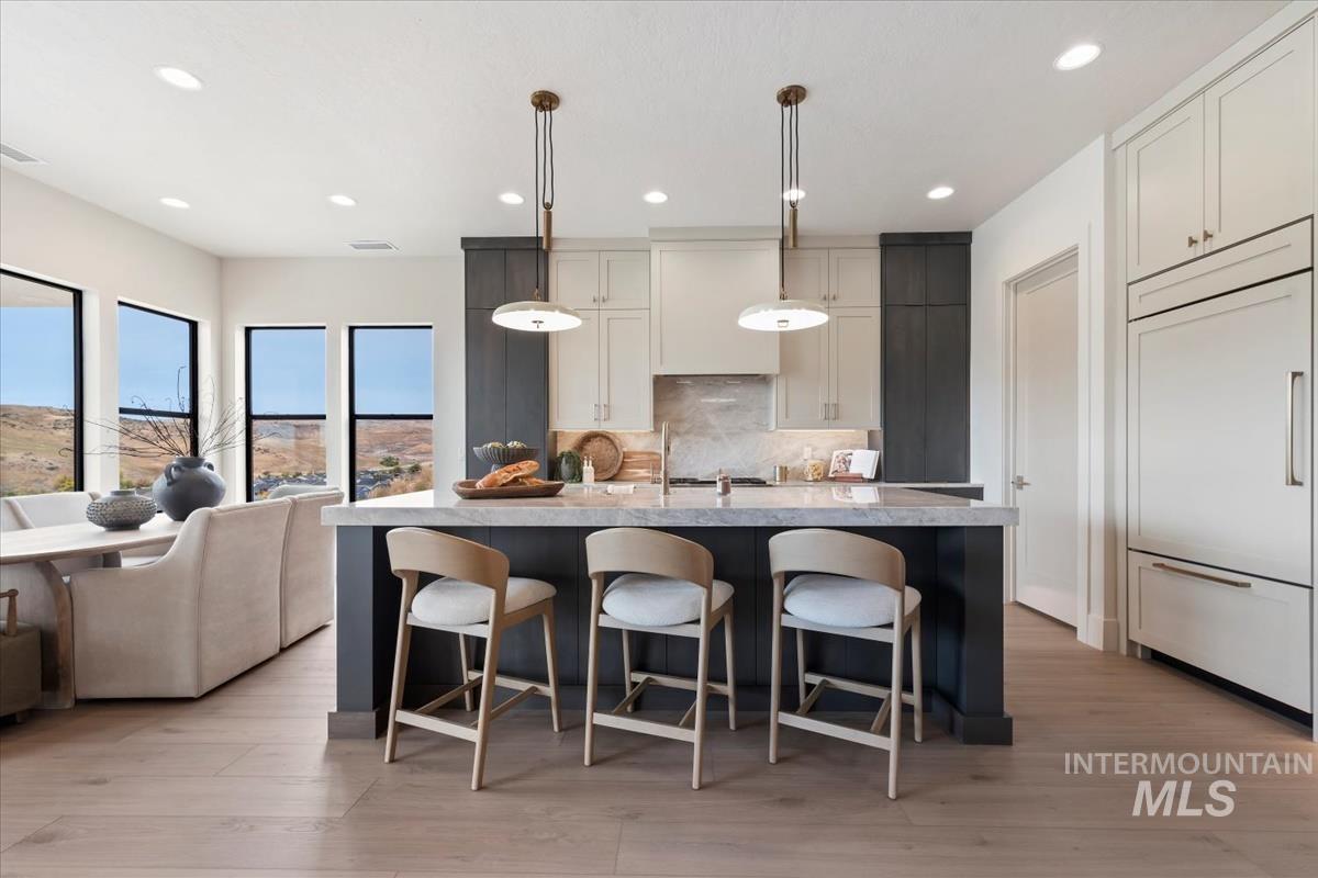 Kitchen featuring decorative light fixtures, a breakfast bar, a center island with sink, paneled built in fridge, and backsplash