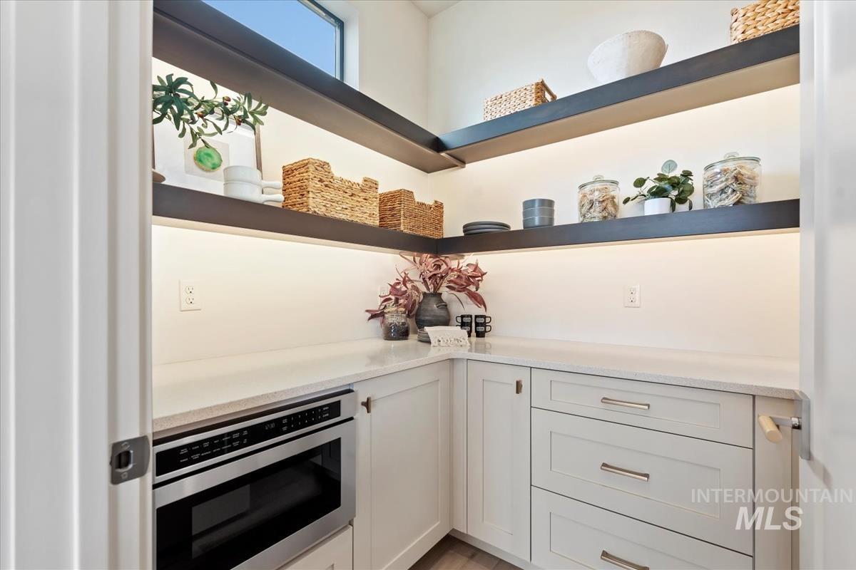 Kitchen with open shelves, white cabinets, light stone counters, and stainless steel microwave