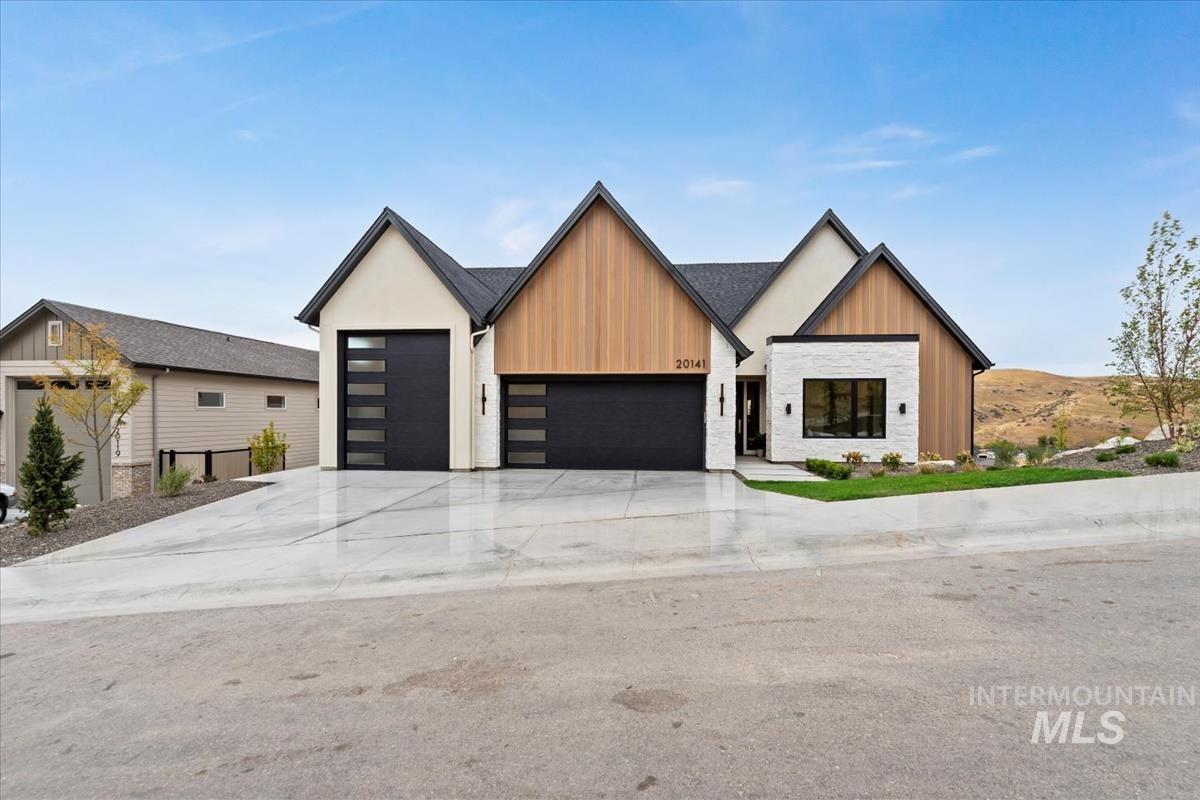 View of front facade with an attached garage, concrete driveway, board and batten siding, and stone siding