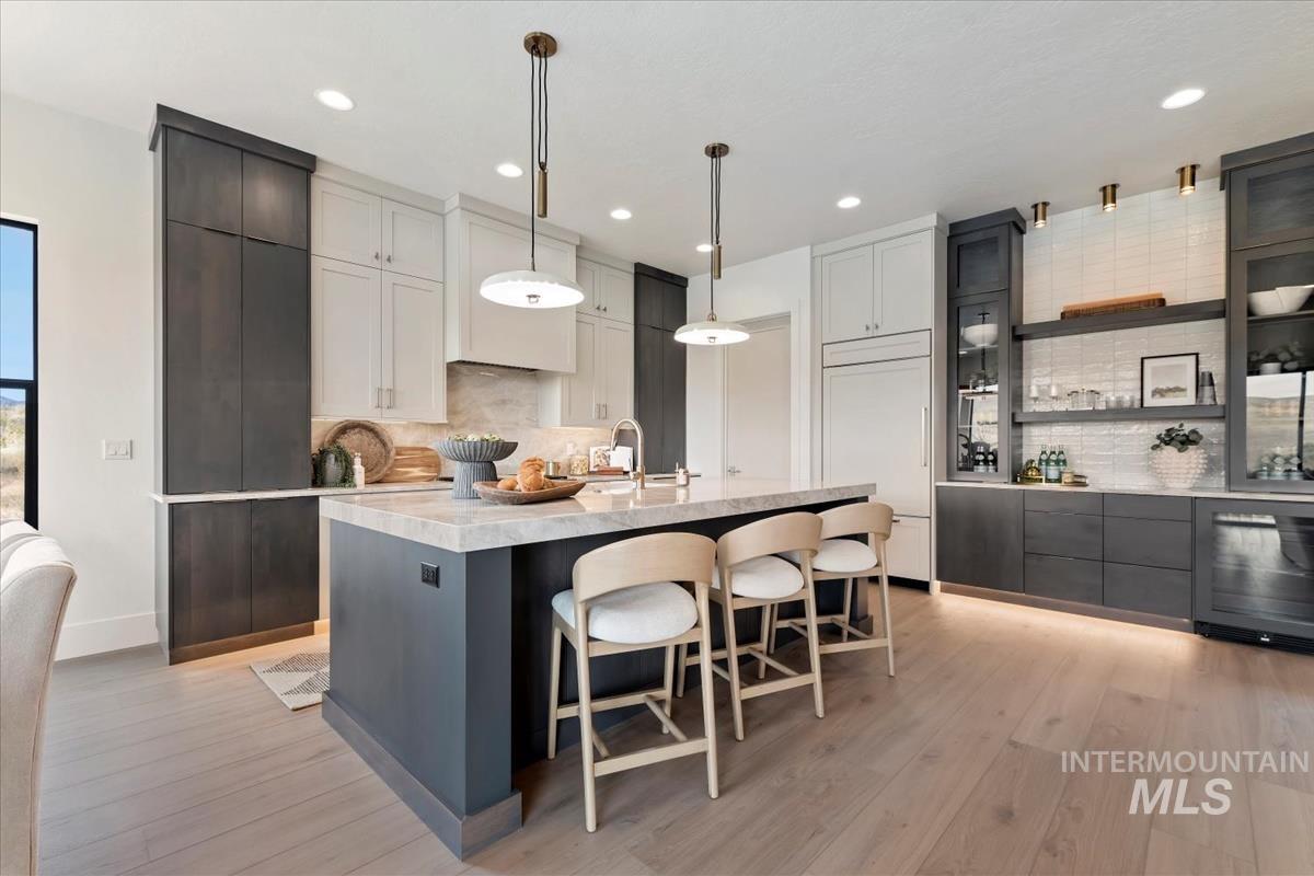 Kitchen featuring a kitchen bar, hanging light fixtures, light stone counters, an island with sink, and backsplash