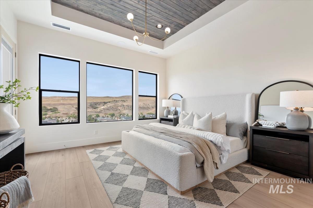 Bedroom with light wood-type flooring, a raised ceiling, wood ceiling, and a chandelier