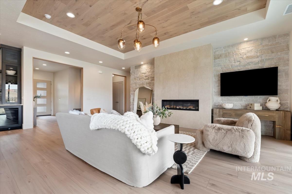 Living room featuring a tray ceiling, a fireplace, recessed lighting, light wood-style flooring, and wood ceiling