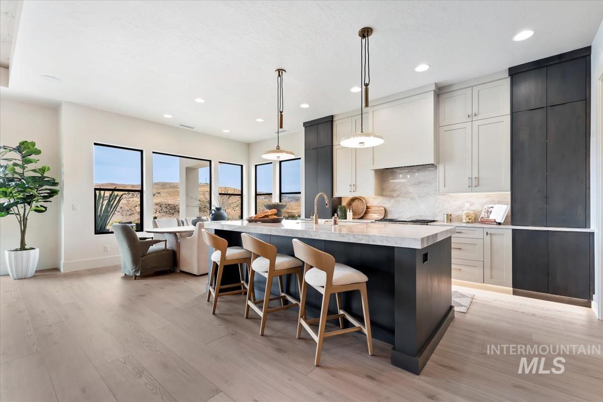 Kitchen with backsplash, hanging light fixtures, light stone countertops, a kitchen island with sink, and recessed lighting